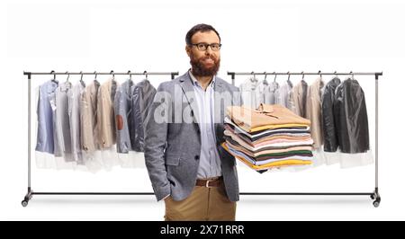 Homme tenant une pile de vêtements pliés devant une étagère avec des vêtements sur cintres isolés sur un fond blanc Banque D'Images