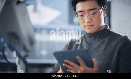Étudiant utilisant la tablette pour contrôler la main robotique. Bras bionique se déplaçant dans différentes directions pendant la classe universitaire. Homme asiatique développant un logiciel pour l'installation de robotique. Concept informatique. Banque D'Images