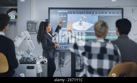 Fille étudiante caucasienne levez la main et demandez à l'enseignant debout près du grand écran. Adolescents qui étudient le bras robotique à la leçon de l'Université moderne de technologie. Concept d'apprentissage automatique Banque D'Images