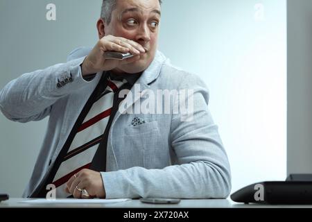 Homme aux cheveux gris piquants, veste de costume gris clair, chemise gris foncé et cravate rayée, sirote nerveusement d'un flacon tout en jetant un coup d'œil sur le côté, apparaissant afr Banque D'Images