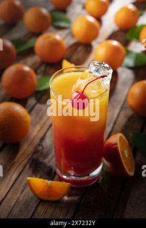 Cocktail classique de tequila au lever du soleil, superposé de tequila aux teintes vibrantes de jus d'orange et de grenadine, garni d'une brochette de cerises maraschino. Banque D'Images