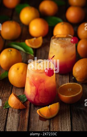 Cocktail classique de tequila au lever du soleil, superposé de tequila aux teintes vibrantes de jus d'orange et de grenadine, garni d'une brochette de cerises maraschino. Banque D'Images