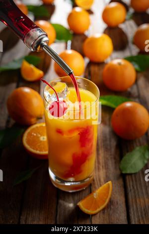 Cocktail classique de tequila au lever du soleil, superposé de tequila aux teintes vibrantes de jus d'orange et de grenadine, garni d'une brochette de cerises maraschino. La grenadine est po Banque D'Images