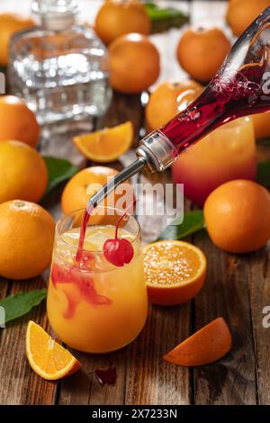 Cocktail classique de tequila au lever du soleil, superposé de tequila aux teintes vibrantes de jus d'orange et de grenadine, garni d'une brochette de cerises maraschino. Banque D'Images