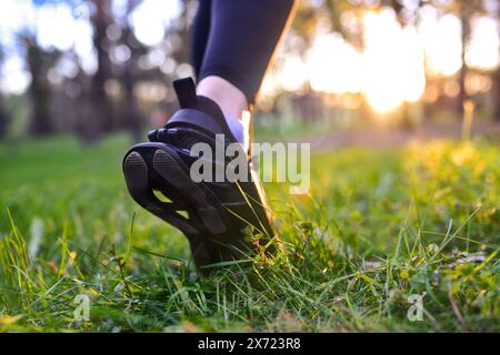 Fermer Voir pieds de femme en baskets noires marchant sur l'herbe dans les bois Banque D'Images