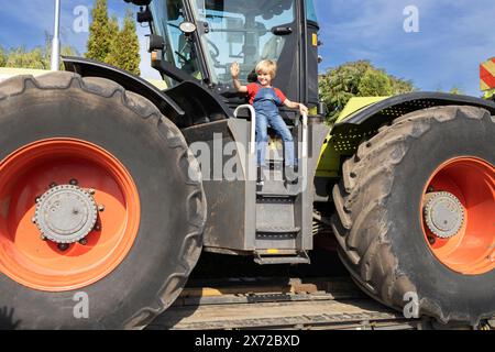 l'enfant est assis heureux sur un énorme tracteur agricole. Équipement pour l'agriculture et l'agrobusiness. L'intérêt du garçon pour les machines et leur travail. Passe-temps pour hommes Banque D'Images