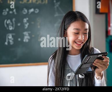 Une fille sourit tout en tenant un téléphone portable devant un tableau noir avec des maths Banque D'Images