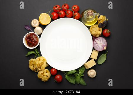 Assiette entourée de différents types de pâtes et de produits sur fond noir, pose plate. Espace pour le texte Banque D'Images