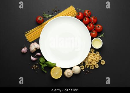 Assiette entourée de différents types de pâtes, produits et grains de poivre sur fond noir, pose à plat. Espace pour le texte Banque D'Images