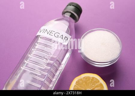 Nettoyants naturels respectueux de l'environnement. Vinaigre en bouteille, citron coupé et bol de soda sur fond violet Banque D'Images