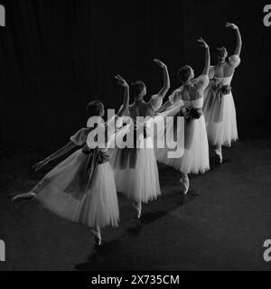 Ballerines jouant élégamment sur scène, les robes coulent gracieusement en étendant leurs bras et leurs jambes à l'unisson. Photo monochrome. Banque D'Images