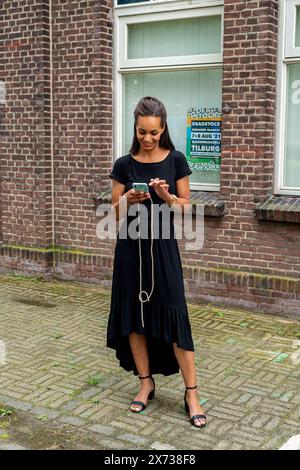 Histoire s Fashion Portrait jeune adulte, créatrice de mode féminine vérifiant son smartphone Messeges. Tilburg, pays-Bas. MRYES Tilburg Spoozone 013 No Banque D'Images