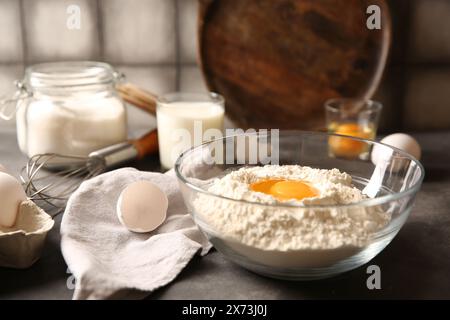 Faire de la pâte. Farine avec jaune d'oeuf dans un bol sur la table grise, gros plan Banque D'Images