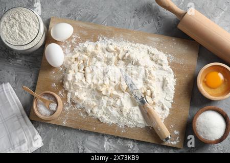 Fabrication de pâte brisée. Différents ingrédients pour la pâte, le couteau et le rouleau à pâtisserie sur la table grise, vue de dessus Banque D'Images