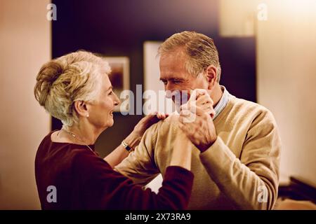Couple senior, heureux et dansant dans la cuisine pour célébrer la date anniversaire, la maison et la conversation. Acclamations, sourire et homme âgé ou femme se liant Banque D'Images