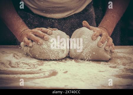 Un boulanger pétrit la pâte à pain dans la boulangerie. Style vintage avec grain. Banque D'Images