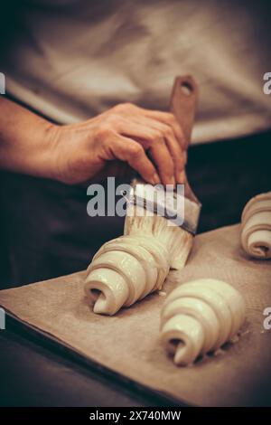 Brossez à la main le beurre liquide ou le glaçage sur les croissants crus, à la verticale. Style vintage avec grain. Banque D'Images