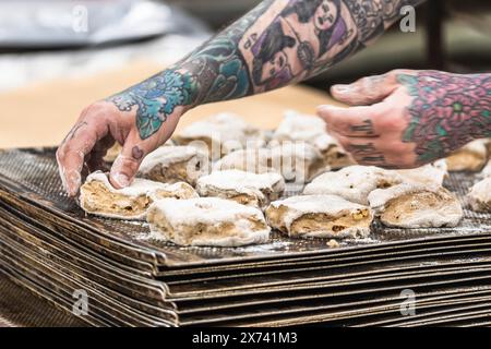 Un boulanger avec des tatouages met des petits pains de pâte crus sur la plaque de cuisson dans la boulangerie Banque D'Images