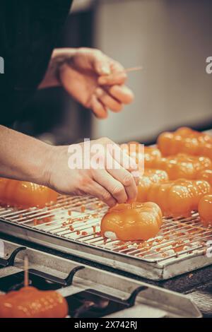 Mains de la confiseuse femelle décorant des tartes glacées orange. Préparation des tartelettes par un pâtissier professionnel. Vertical. Banque D'Images