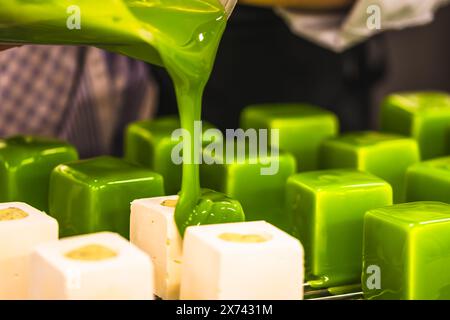 Le confiseur recouvre les tartelettes d'un glaçage vert. Préparation des tartelettes par un pâtissier professionnel. Banque D'Images