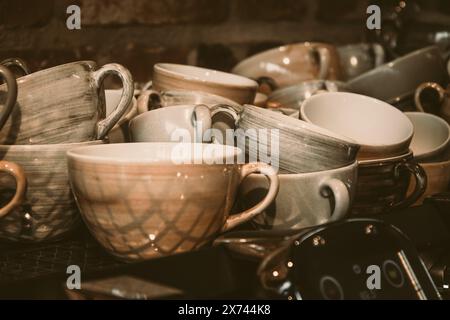 Tasses à café empilées en faïence brun brillant et gris sur une machine à café devant un mur de pierre Banque D'Images