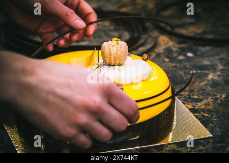 Mains de confiseur décorant la tarte jaune avec du chocolat. Banque D'Images