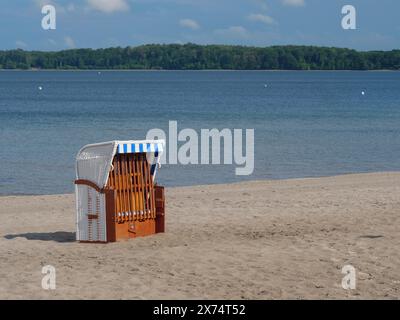 Une chaise de plage vide se dresse sur la plage de sable d'un lac sous un ciel bleu avec quelques nuages, chaise de plage solitaire sur une plage tranquille avec un arbre dans le Banque D'Images