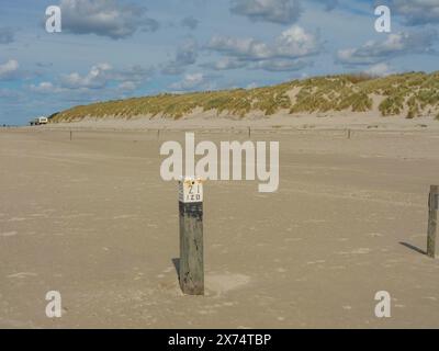 Zone côtière sablonneuse avec des dunes couvertes d'herbe et un poteau au premier plan, nuages sur la plage avec des dunes au bord de la mer, hollum, ameland, pays-bas Banque D'Images