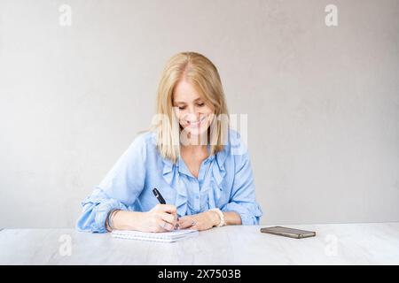 Belle femme souriante mi-adulte écrit dans son cahier Banque D'Images