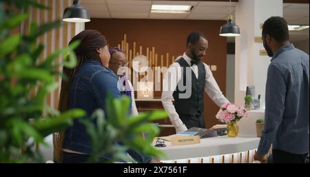 Réceptionniste effectuant l'enregistrement pour les clients, aidant les voyageurs à se détendre après un long vol et voir l'hébergement. Jeune couple bénéficiant d'un service de conciergerie luxueux au refuge de vacances cinq étoiles. Banque D'Images