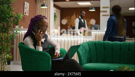 Dans le salon de l'hôtel, concierge travaillant sur ordinateur portable et répondant aux appels pour les réservations à distance. Le membre du personnel de la station cinq étoiles gère l'assistance téléphonique et les inscriptions. Banque D'Images