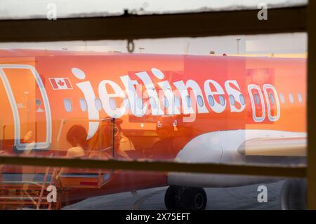 Miami, Floride, États-Unis - 03 14 2024 : le fuselage orange avec des lettres blanches de l'Airbus A320 de Canada Jetlines vu à travers une fenêtre réfléchissante Banque D'Images