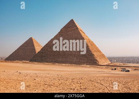 Les pyramides de Khafre et Menkaure s'élèvent du plateau de Gizeh sous un ciel clair, avec un premier plan du désert et la périphérie du Caire faiblement visible dans le Banque D'Images