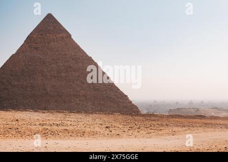 Vue latérale de la Grande Pyramide de Gizeh s'élevant des sables du désert, avec un ciel brumeux et une vue lointaine sur le paysage environnant Banque D'Images