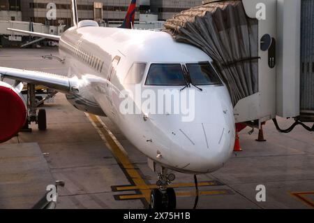 Vue de face d'un avion de ligne moderne blanc avec passerelle d'embarquement des passagers attachée. L'avion est assis sur un tarmac en béton avec des lignes de voie peintes Banque D'Images