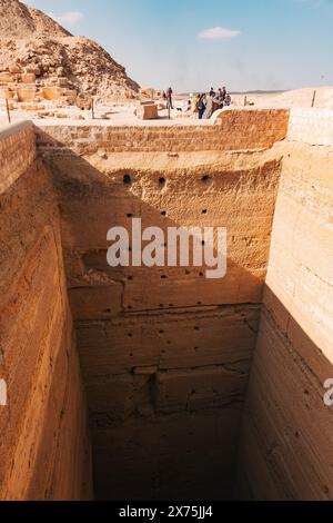 Puits vertical massif à la nécropole de Saqqara, probablement partie d'un complexe funéraire ou d'une excavation de tombeau, avec des visiteurs observant d'en haut sous le désert Banque D'Images