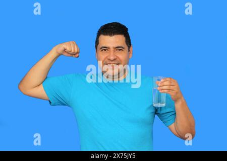 L'homme adulte latino à la peau foncée montre son verre avec de l'eau plate pour s'hydrater par temps chaud Banque D'Images