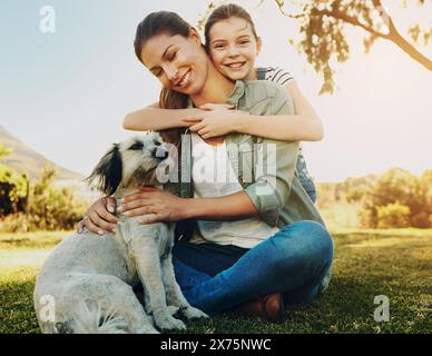 Mère, fille et jouer avec le chien dans le parc pour se lier, se détendre et heureux avec l'activité amusante dans la nature. Famille, femme et fille avec chiot sur l'herbe dans Banque D'Images