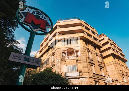 Vue en bas angle d'un panneau de la station Cairo Metro Green Line 3 devant un immeuble historique jaune de plusieurs étages avec balcons décorés Banque D'Images