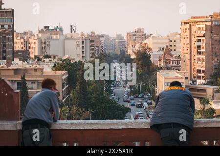 Les gardes de sécurité s'appuient sur la balustrade en grès rouge du Palais du Baron Empain, surplombant les rues urbaines animées d'Héliopolis, au Caire, au crépuscule Banque D'Images