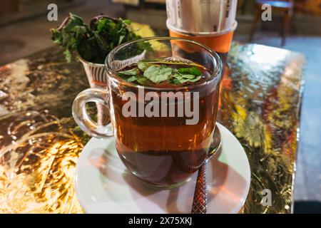 Thé à la menthe égyptien traditionnel servi dans une tasse en verre sur une table de café, capturant l'ambiance chaleureuse et la culture locale du thé Banque D'Images