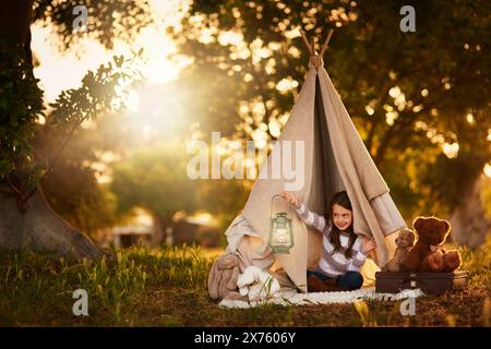 Tipi, enfant et plaisir dans la tente de jardin en plein air dans la nature pour le camping, le jeu et l'aventure avec la lumière du soleil. Tissu, lampe et maison de fantaisie pour fille dans Banque D'Images