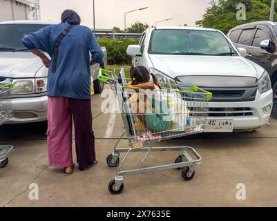 Un client d'un grand magasin est debout dans le parking avec un enfant dans un panier Banque D'Images