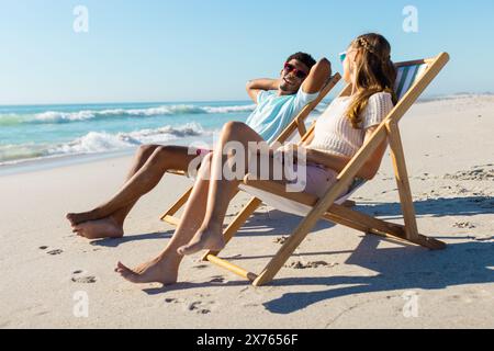 À la plage, couple diversifié se relaxant sur des chaises, profitant du soleil Banque D'Images