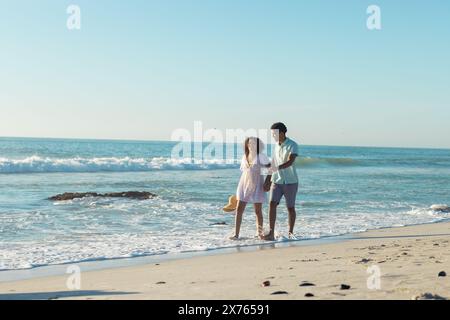 À la plage, couple biracial marchant, mâle embrassant femelle par derrière Banque D'Images