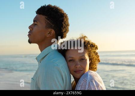 A la plage, couple biracial debout, femme appuyée sur l'homme Banque D'Images