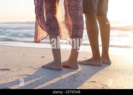 À la plage, couple biracial debout, profitant du coucher du soleil Banque D'Images