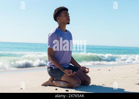 À la plage, jeune homme biracial assis, pratiquant la méditation Banque D'Images