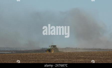 Un tracteur israélien se déplace le long de la frontière avec la bande de Gaza alors que la fumée affluait massivement après une frappe israélienne sur le Nord de Gaza au milieu des combats continus entre Israël et le groupe militant Hamas le 17 mai 2024 à la frontière de Gaza, en Israël. Banque D'Images