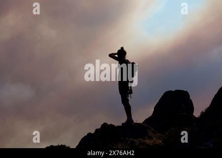 Randonneur observant de loin depuis le sommet du Roc'h Bichourel le feu dans les Monts d'Arrée au-dessus de Brasparts pendant le feu de 18 juillet 2022. Banque D'Images